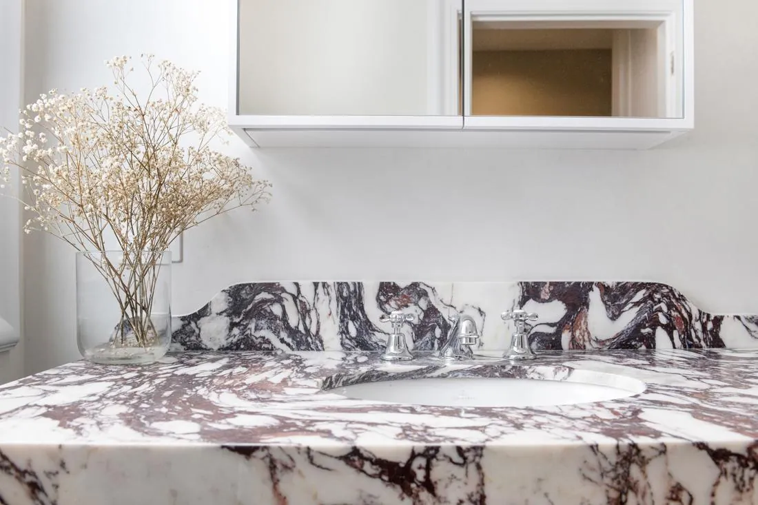 Bathroom vanity with a marble countertop, chrome faucet, and a glass vase of dried flowers beside the sink.
