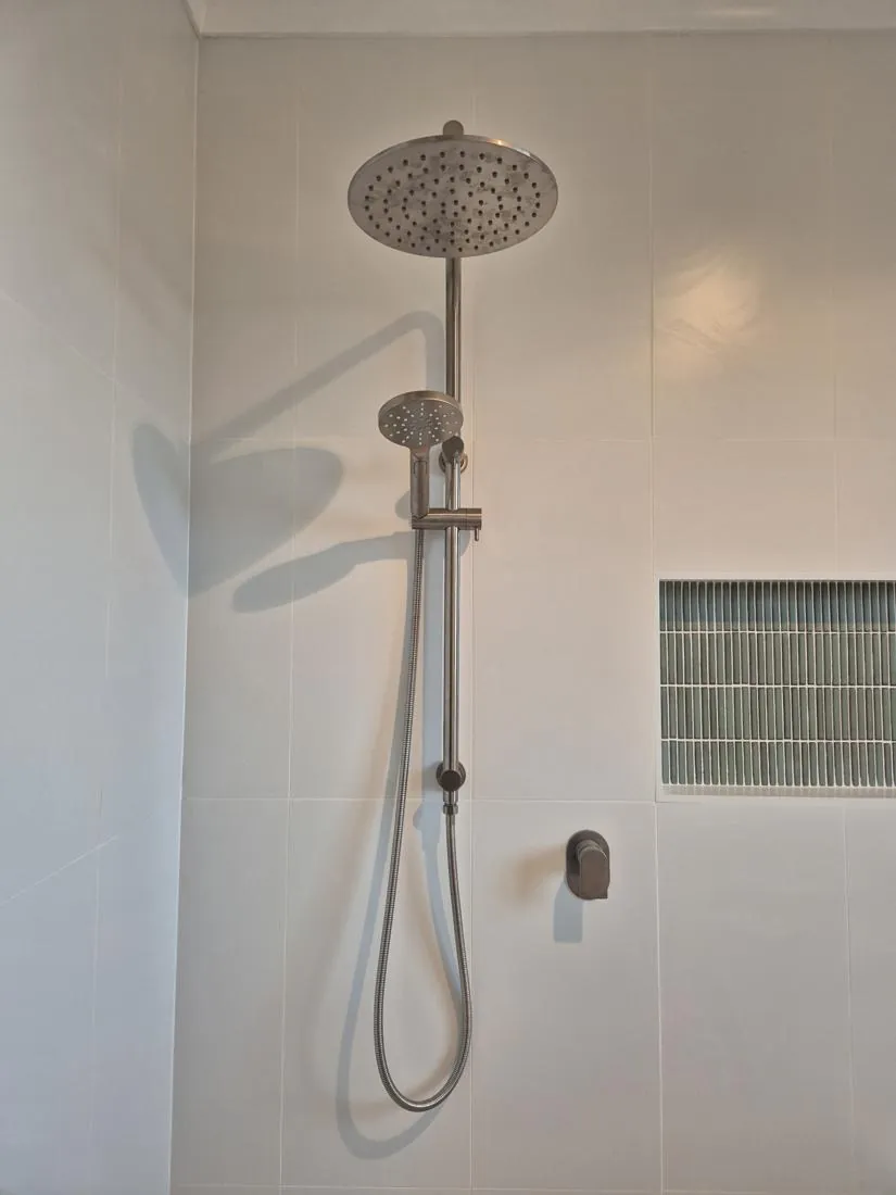Modern shower with a large rainfall head overhead and a handheld wand on a chrome rail against white tile walls, with a flexible hose.