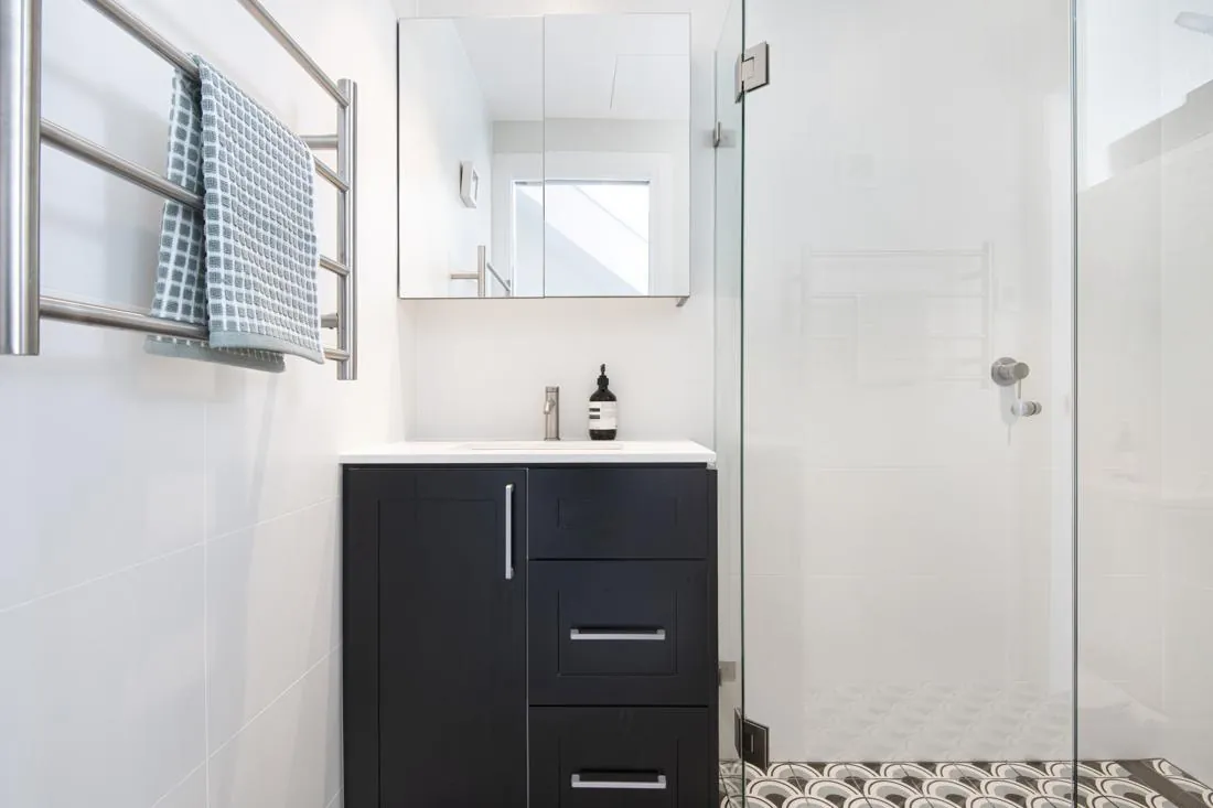 Modern bathroom with a dark blue vanity, white countertop, mirrored cabinet, and a glass shower enclosure.