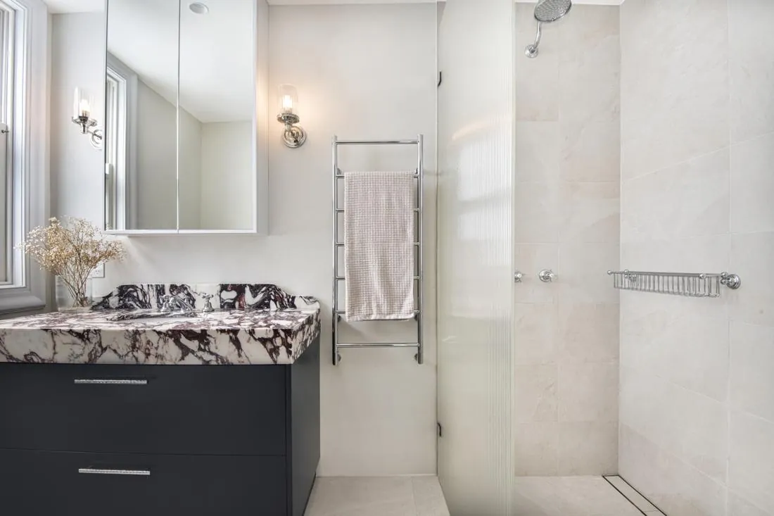 Modern bathroom with a marble-veined countertop vanity, dark gray drawers, and a chrome towel warmer.